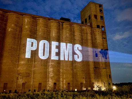 A photograph of the word "poems" in white text projected onto the side of a brown building.